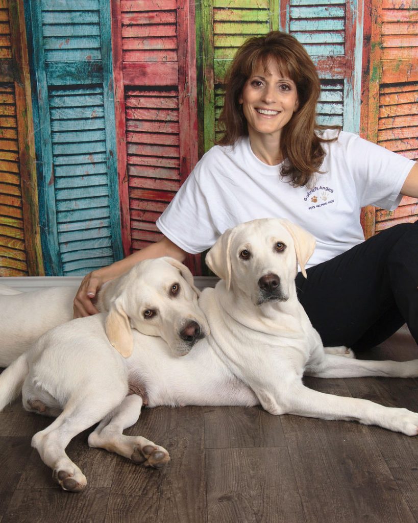 Sandy sitting with two of her white labrador puppies laying on the floor.